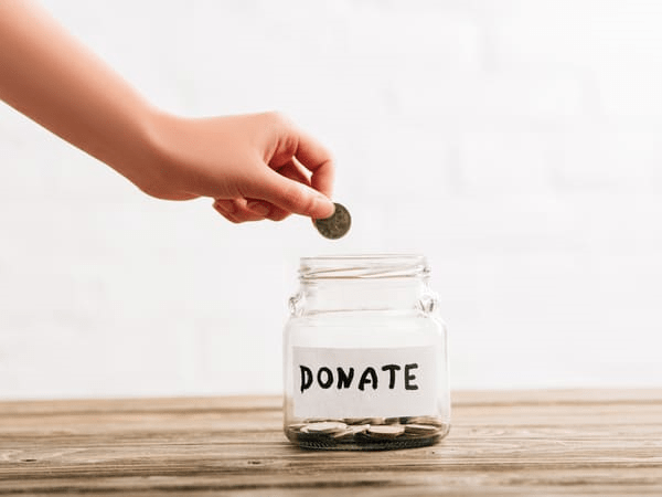 A hand puts a coin in a jar that says “Donate.”